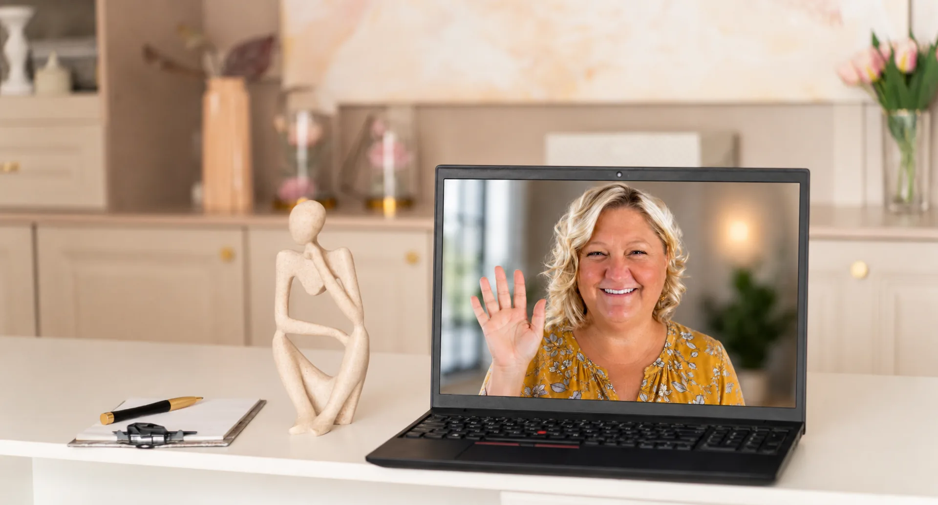 Wendi waving hello on a laptop screen in a bright, welcoming kitchen — ready for a virtual session.